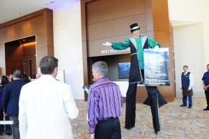 Tall man greets guests and press holding a menu of the complimentary eats.