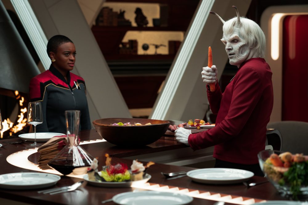 Uhura meets Hemmer as Hemmer chops carrots in episode 2 of Star Trek: Strange New Worlds. In the background you can see a shelf with Pike's Captain's trinkets.