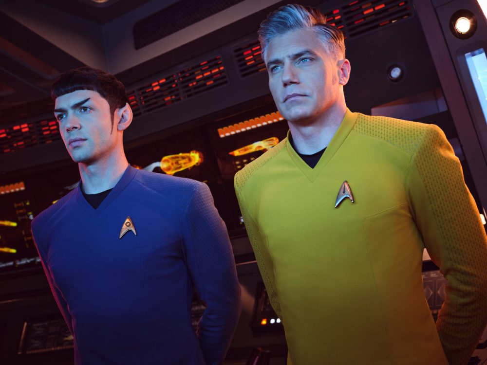 Spock and Pike in uniform, standing at attention beside one another on the bridge of the Enterprise, on Star Trek: Strange New Worlds.