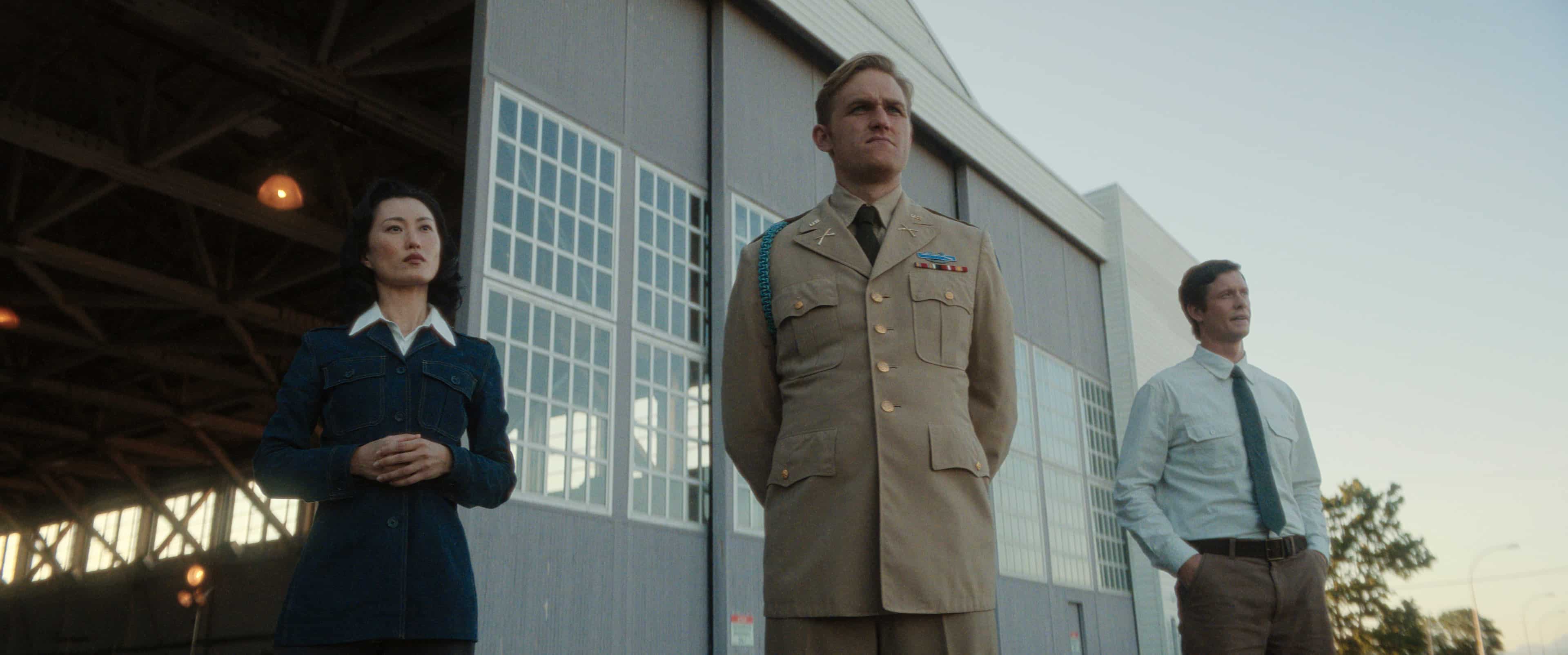 Mari Yamamoto, Wyatt Russell and Anders Holm in Monarch: Legacy of Monsters. They are wearing 50s clothes and standing in front of a large hanger.