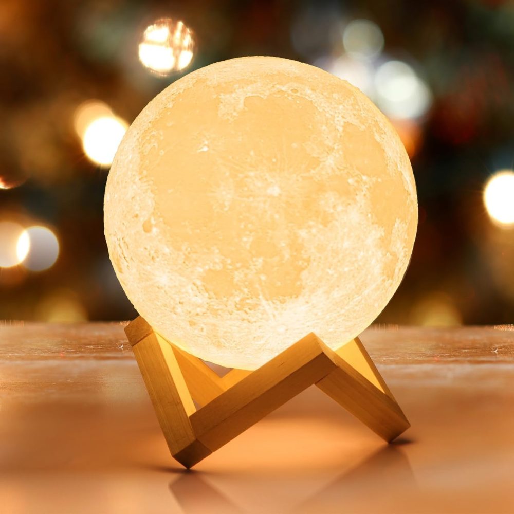 A lamp in the shape of the moon glows pale orange and rests on a wooden base