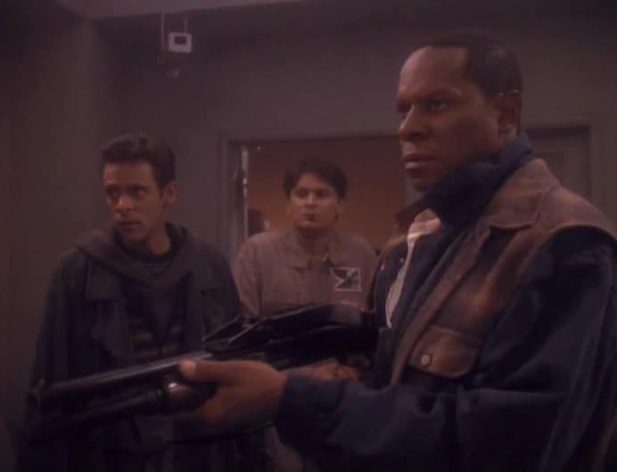 Julian Bashir (Alexander Siddig) and Ben Sisko (Avery Brooks) at a Sanctuary processing center in San Francisco, 2024. They are both wearing 21st century clothing. Sisko holds a rifle. From Star Trek: Deep Space Nine, "Past Tense."