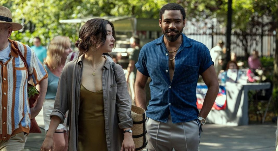Maya Erskine, an Asian woman dressed in a brown and grey, and Donald Glover, a Black man with short hair wearing a blue shirt, as Mr. & Mrs. Smith