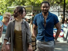 Maya Erskine, an Asian woman dressed in a brown and grey, and Donald Glover, a Black man with short hair wearing a blue shirt, as Mr. & Mrs. Smith
