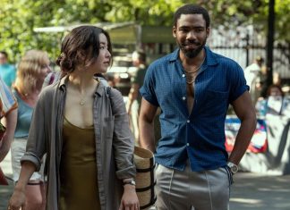 TV Review: MR. & MRS. SMITH hits its target in a fun reinterpretation Maya Erskine, an Asian woman dressed in a brown and grey, and Donald Glover, a Black man with short hair wearing a blue shirt, as Mr. & Mrs. Smith