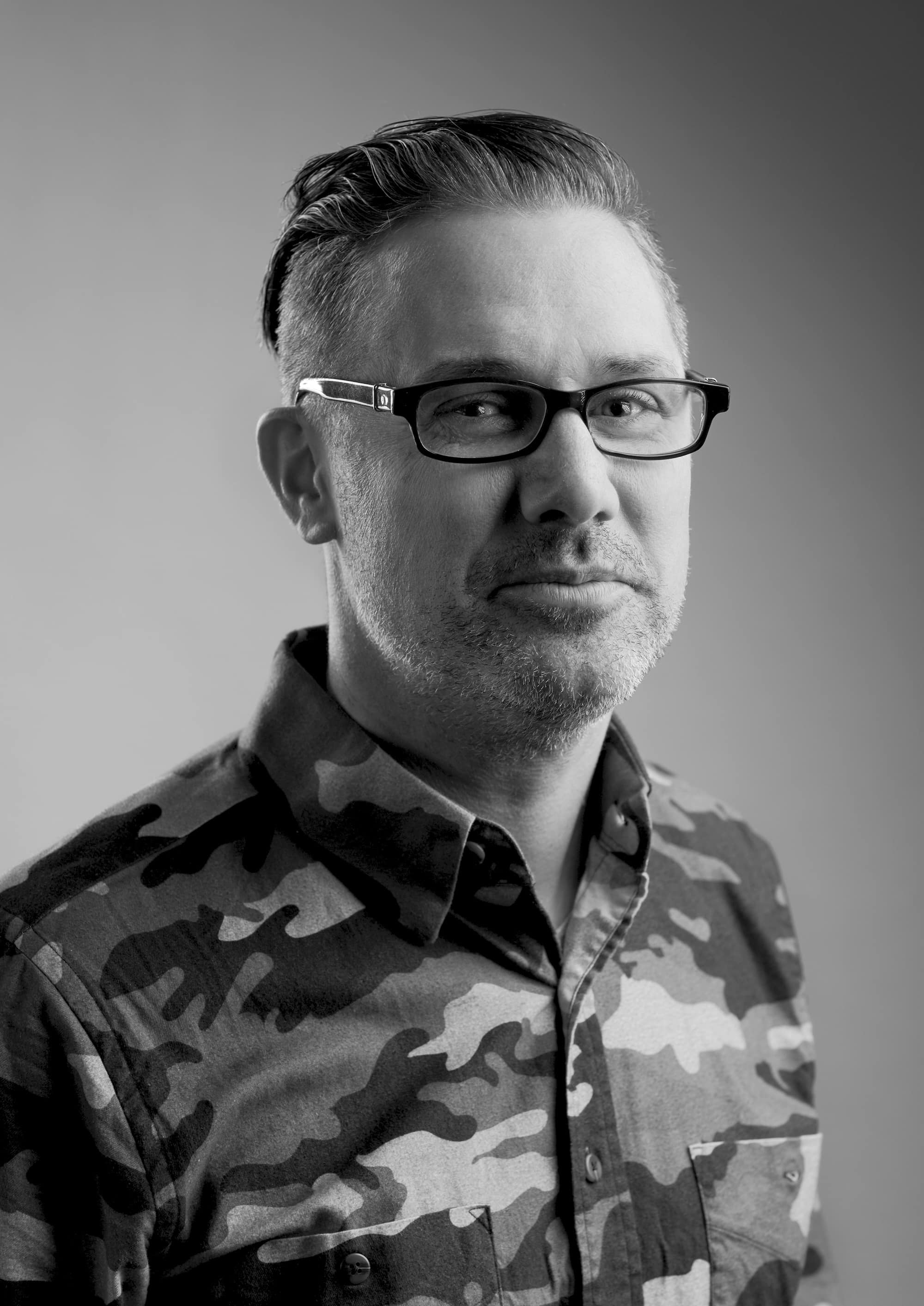Kirk Benshoff headshot. Image depicts man in glasses with short hair and camouflage button down.