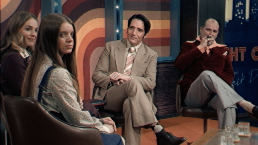 An interview scene from Late night with the Devil. Actress Ingrid Torrelli looks into the camera while Laura Gordon, David Dastmalchian, and Ian Bliss sit in the background
