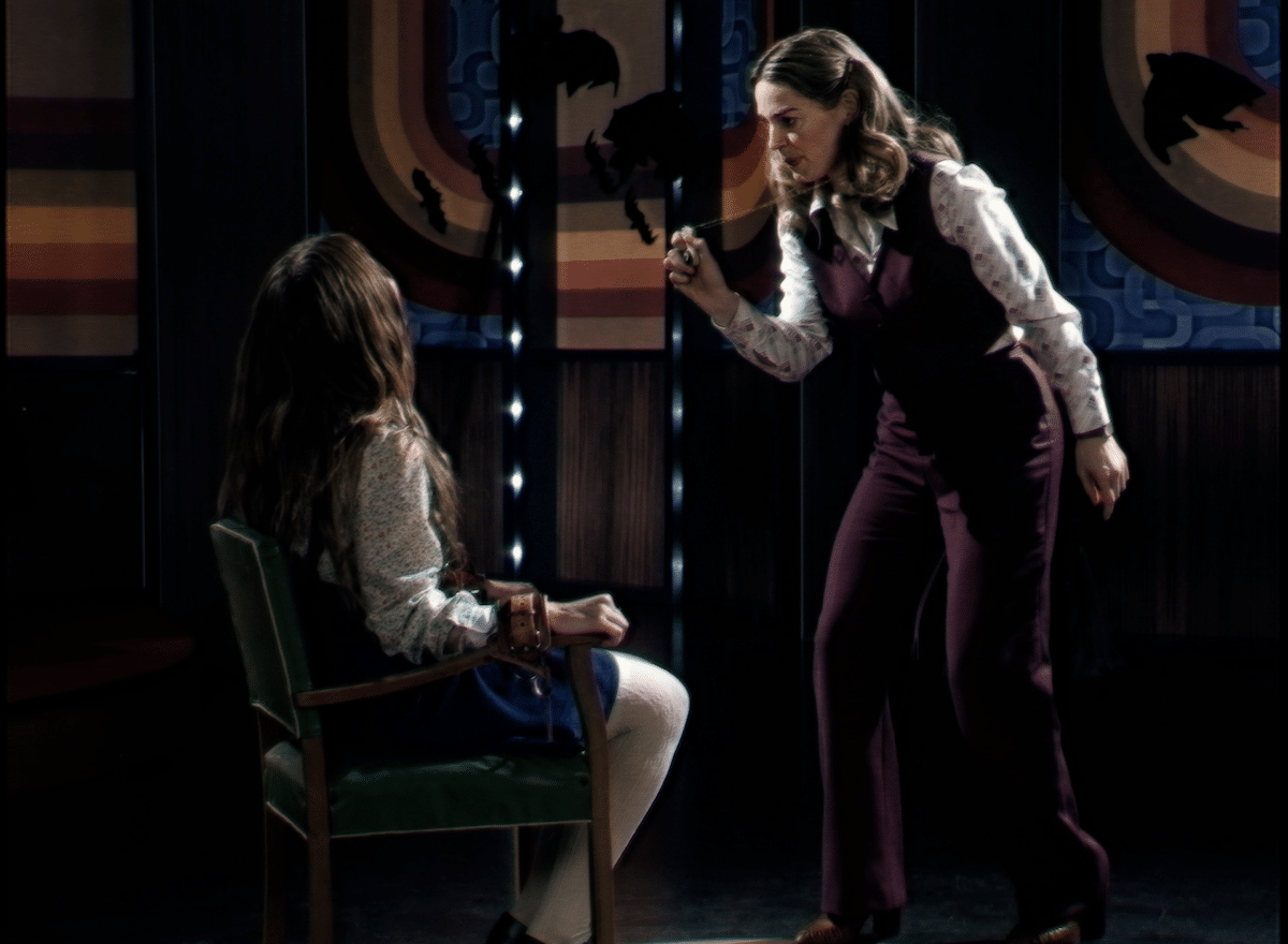 Doctor June Ross-Mitchell (played by Laura Gordon) talks to a possessed Lily (played by Ingrid Torrelli) in low studio lighting