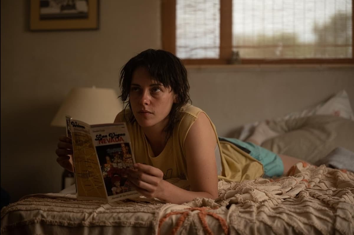 Kristen Stewart lies on a bed reading a pamphlet about Las Vegas