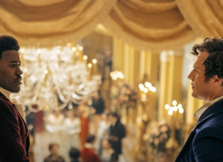 TV Review: DOCTOR WHO’s ‘Rogue’ steals more hearts than just the Doctor’s The Doctor (portrayed by Ncuti Gatwa, a black man with his hair tied back, wearing a plum waistcoat and white trousers,) speaks with the mysterious brooding stranger on the balcony (portrayed by Jonathan Groff, a white man with short brown hair wearing a blue waistcoat.)