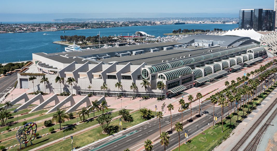 An aerial view of the San Diego Convention Center, a large white brutalist structure with glass by the harbor.