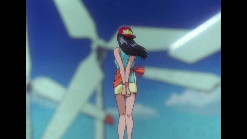 Macross Plus. A young woman wearing a hat and a jacket tied around her waist looks away from the audience towards white wind turbines.