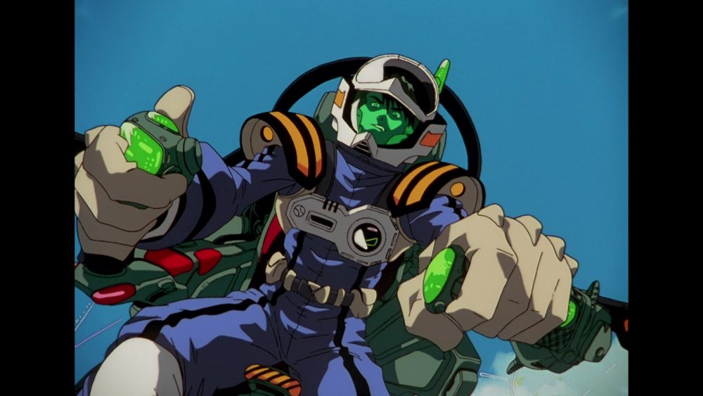 Macross Plus. Man sits in cockpit of experimental fighter jet. He wears blue and chrome fighter gear with a green transparent faceplate.