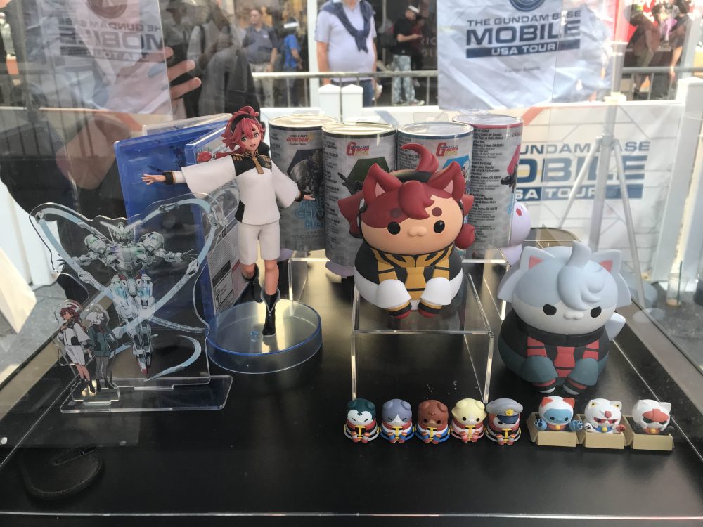 Acrylic Standee of Suletta Mercury and Miorine with the calibarn next to a cat figure of Sulette and Miorine available during the Gundam Base Mobile Tour.