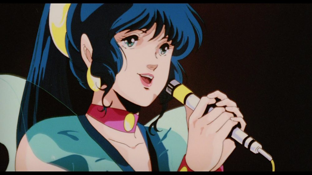 macross do you remember love: pop singer with black hair, yellow hairband+earrings and pink choker sings into microphone