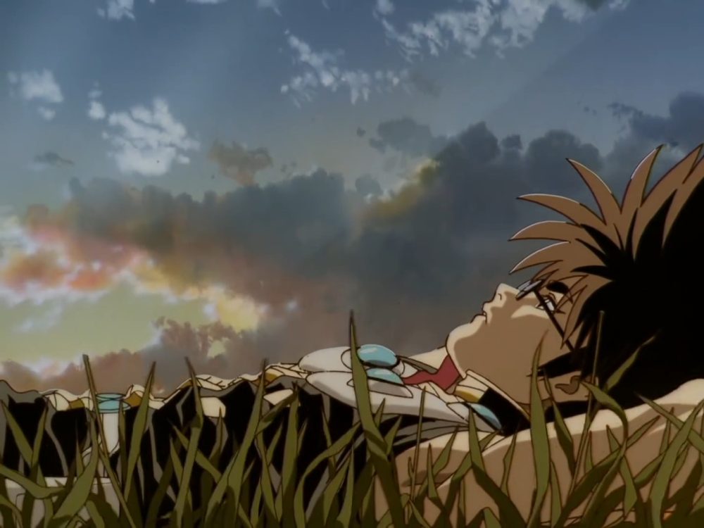spiky-haired young man in glasses lays down in grass