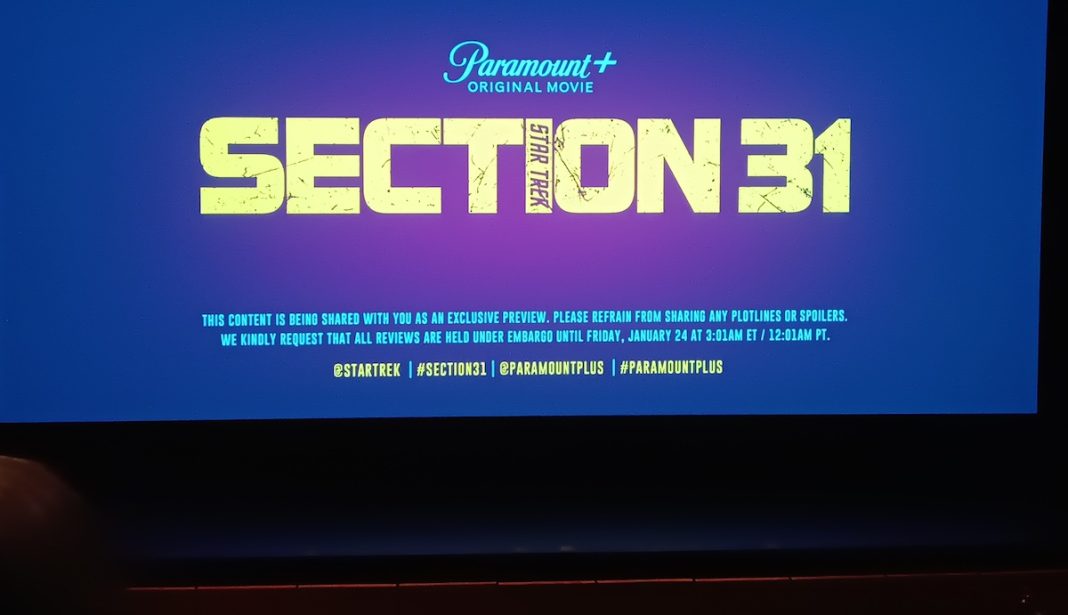 A movie screen that displays the logo for Section 31 with a row of theater seats in the foreground.