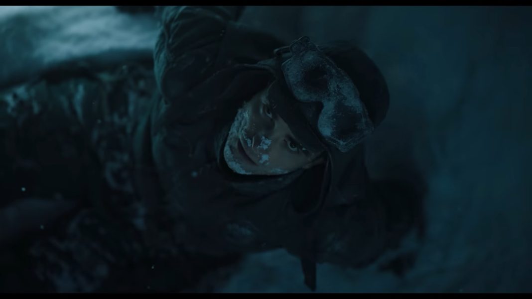 mickey 17 header. shot from above of man wearing snow gear and staring up at camera