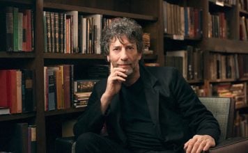 Gaiman breaks year-long silence, claiming blog exonerates him Neil Gaiman is sitting on a chair with rows of books behind him