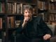 Gaiman breaks year-long silence, claiming blog exonerates him Neil Gaiman is sitting on a chair with rows of books behind him