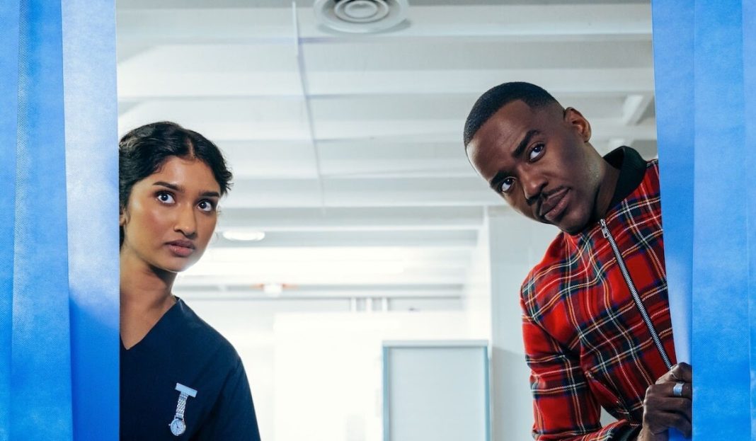 The Doctor (Ncuti Gatwa) and the Nurse, Belinda Chandra (Varada Sethu) peak behind a pair of blue curtains.