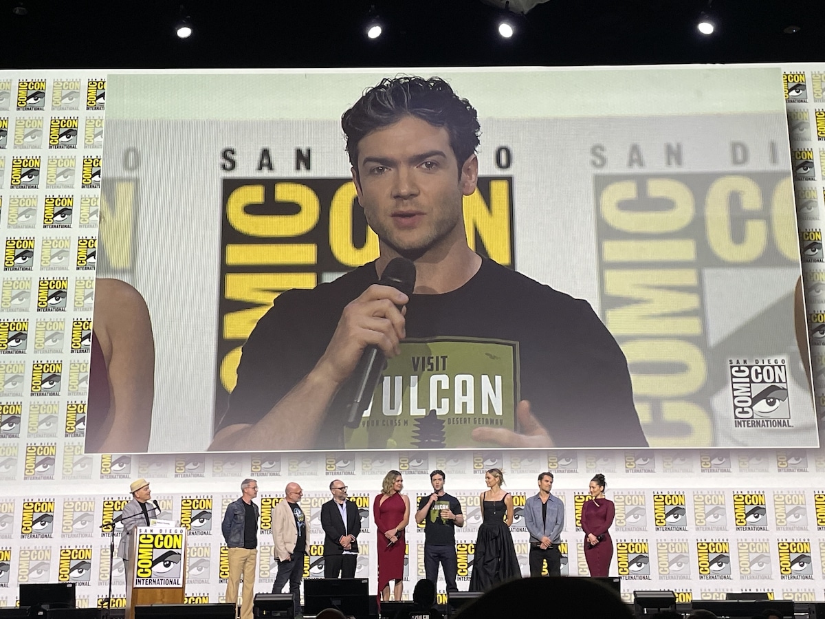 The Strange New Worlds cast and crew onstage in Hall H during the Star Trek Universe panel, with Peck wearing a Vulcan t-shirt on the big screen behind them.