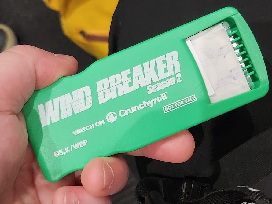 hand holding the green wind breaker season 2 bandaid dispenser, white text with the wind breaker season 2 logo and the text "watch on crunchyroll" and "not for sale" written on it