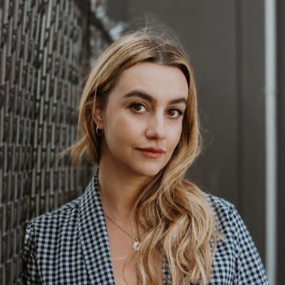 portfolio image of Alessandra Ferreri, head of content at Wattpad wearing a black and white patterned dress shirt while leaning against a chain-linked fence.