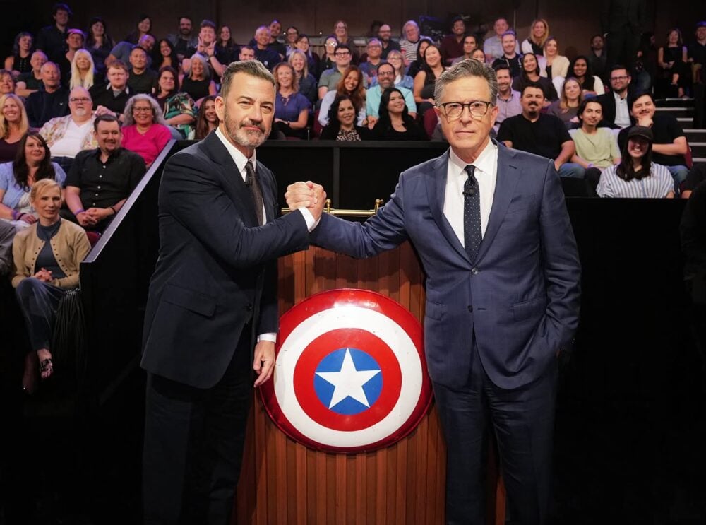 Stephen Colbert and Jimmy Kimmel clasping hands after placing Mark Gruenwald's Captain America shield on the set of Jimmy Kimmel Live!
