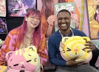 NYCC ‘26: Kim-Joy discusses QUIET graphic novel and bringing baking and mental health into graphic novels The Beat reporter Aaron Halls and Kim-Joy seated at artist alley at NYCC '26 to discuss Quiet smiling and holding plushies.