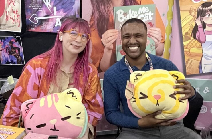 The Beat reporter Aaron Halls and Kim-Joy seated at artist alley at NYCC '26 to discuss Quiet smiling and holding plushies.