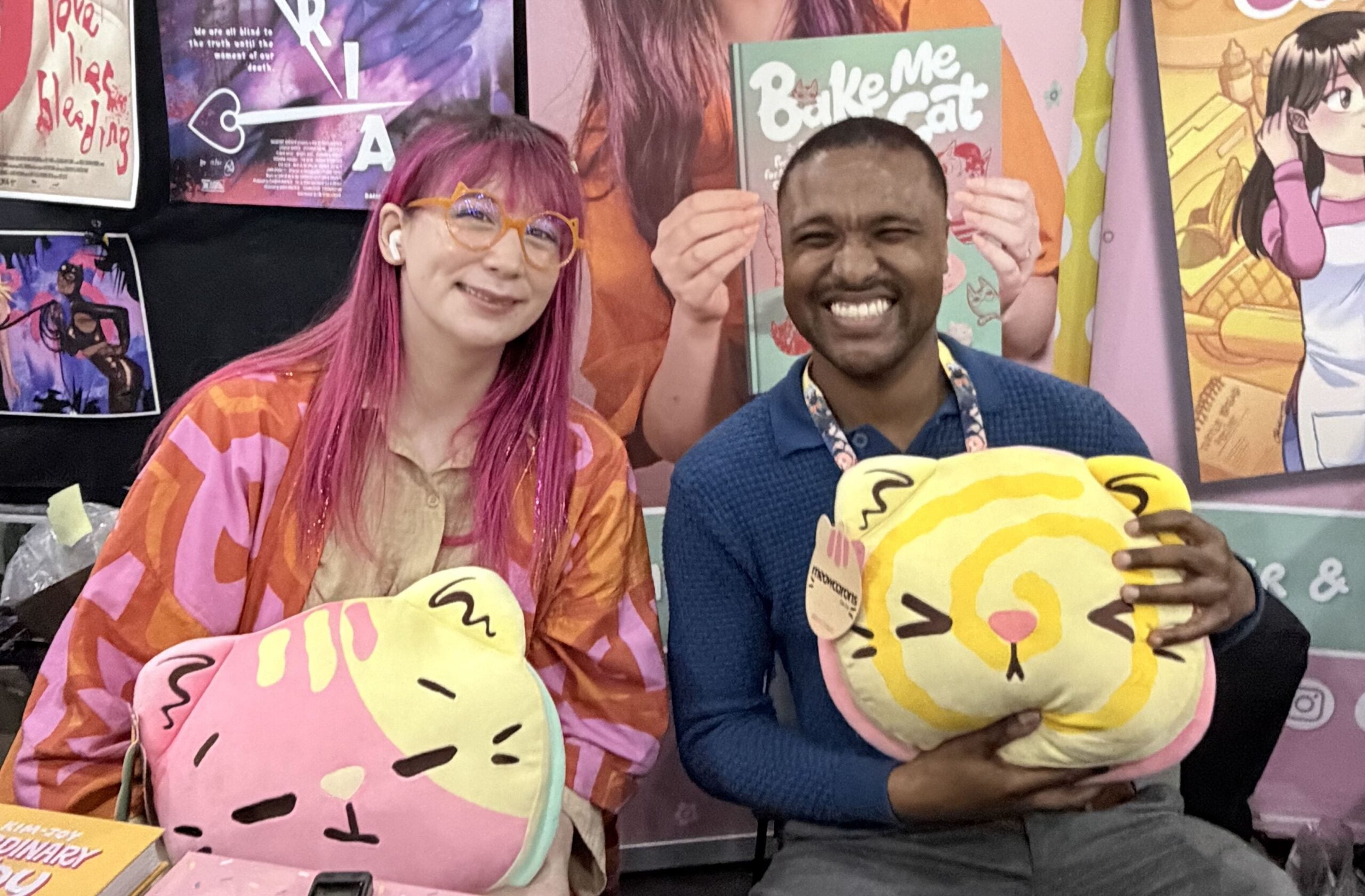 IMG_1001 (1) The Beat reporter Aaron Halls and Kim-Joy seated at artist alley at NYCC '26 to discuss Quiet smiling and holding plushies.